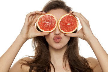 Young sexy woman posing with slices of red grapefruit on her face on white background
