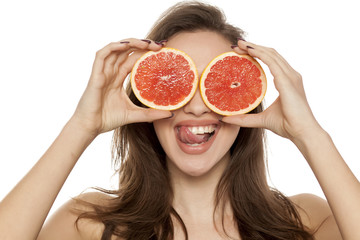 Happy young woman posing with slices of red grapefruit on her face on white background