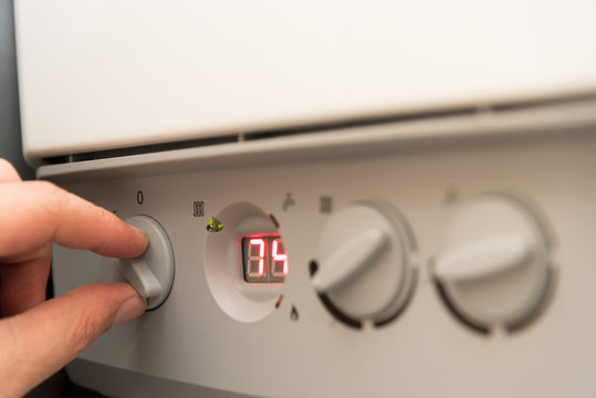 Fingers of a adult man turning on a British Combi Gas Boiler