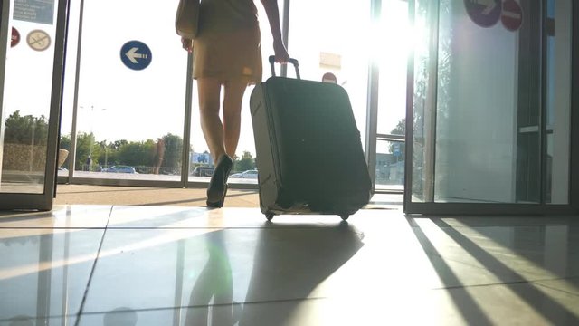 Business lady going from the airport with her luggage. Woman in heels walking with her suitcase through glass doors from terminal to parking of taxi. Trip or vacation travel concept. Slow motion