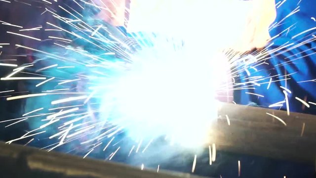 Industrial Worker at the factory welding close up. Electric wheel grinding on steel structure in factory. Welding work
