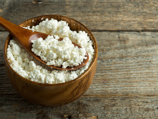 Homemade cottage cheese in a wooden bowl with a spoon on a rustic wooden table.