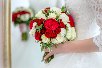 The bride holds a bouquet of red and white roses 
