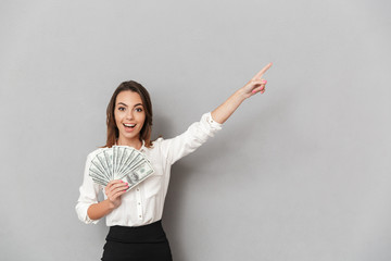 Excited cheerful young business woman looking camera holding money pointing.