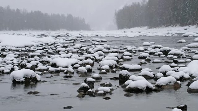 Stones with snow caps in the water of Altai Biya river under heavy snow in winter season
