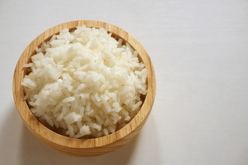 Cooked Jasmine rice in a wooden bowl on a white background.