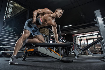 Fototapeta na wymiar muscular young man lifting weights in gym on dark background.
