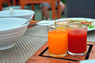 Three glasses with freshly squeezed juices: tomato, mango, orange stands on an old wooden dining table.