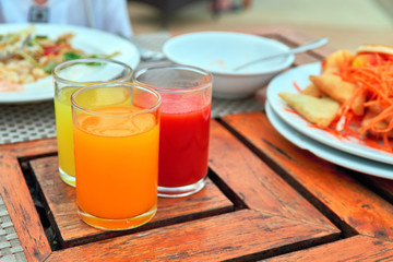 Three glasses with freshly squeezed juices: tomato, mango, orange stands on an vintage wooden table.