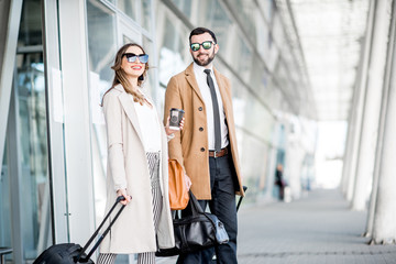 Business couple in coats walking out the airport with luggage during the business trip