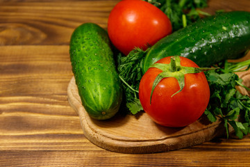 Fresh tomatoes, cucumbers, parsley and dill on cutting board on wooden table