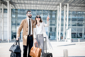 Business couple in coats standing near the airport with luggage during the business trip