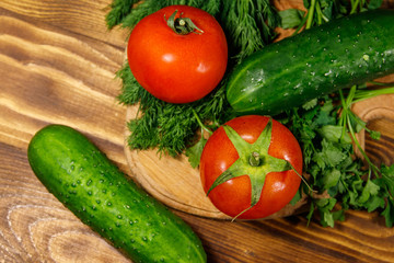 Fresh tomatoes, cucumbers, parsley and dill on cutting board on wooden table