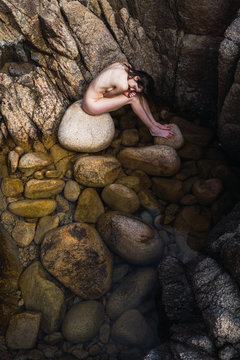Naked woman sitting on stones