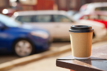 Cardboard cup of coffee on window sill. Blurred car parking on background.