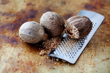 Making nutmeg powder process. Nuts silver grater. Kitchen still life photo. Shallow depth of field, aged brown rusty background. Selective focus. - obrazy, fototapety, plakaty