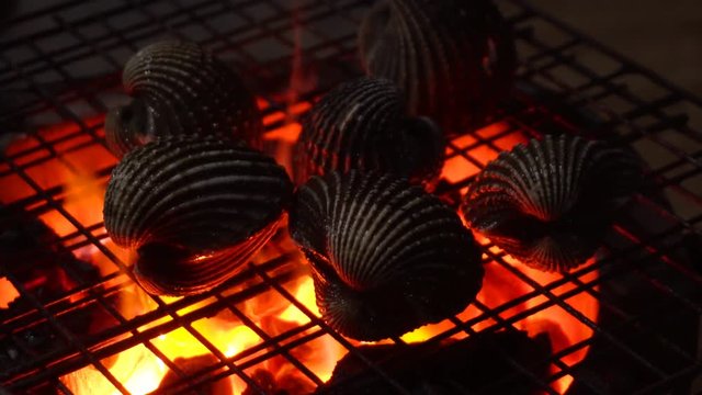 Close up of process cooking seafood on a barbecue with red fire on an asian night market