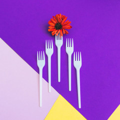 Plastic forks with orange flower on yellow and  purple background of paper textures. Minimal flat lay. surreal food concept of meal