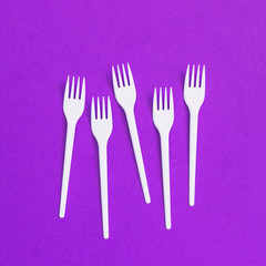 Plastic forks on  purple background of paper textures. Minimal flat lay. Creative concept of food and meal