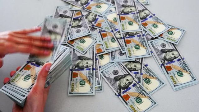 Dollar bills, money background. Hands flipping through a stack of US dollar bills with a large stack of hundred US dollar bills on background.