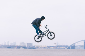 The Young BMX reader makes the Barzpin trick against the background of the city skyline. BMX concept. Tricks on the minimalist background.BMX freestyle