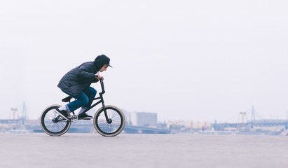 Street culture. Young BMX rider riding a bike on a minimalist city background. BMX cyclist is going...