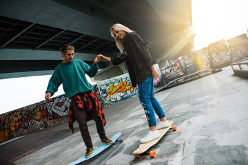 Extreme lesson. Young handsome men teaching his girlfriend how to ride longboard in skateboard park outdoors