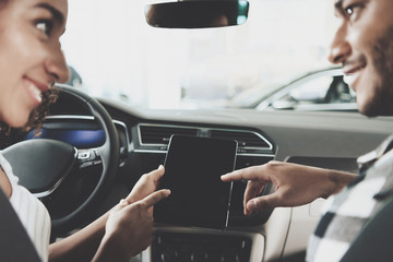 African american family at car dealership. Mother and father are using tablet in new car.