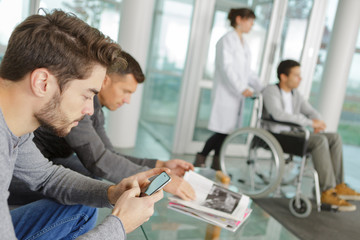Fototapeta premium Man using smartphone in hospital waiting area