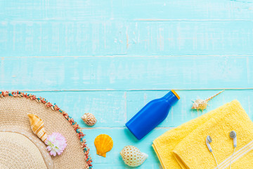 Beach accessories including sunglasses, sunscreen, hat beach, shell, yellow towel and Earphone on bright blue pastel wooden background for summer holiday and vacation concept.