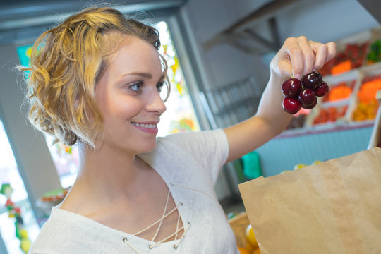 cheerful happy young woman selecting cherries at store