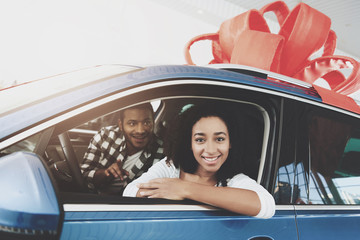 African american family at car dealership. Mother and father are sitting in new car with ribbon on top.