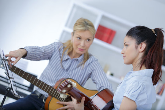 mature female teaching her student how to play guitar - Powered by Adobe