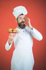 Male chef with beard and mustache with plate of oatmeal cookies shows sign delicious. Bearded chef showing OK sign. Baker, chef or cook holds plate with oatmeal cookies with taste approval gesture.