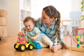 Little child boy and mom playing on the floor with tractor toy