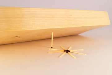 A thin wooden match supports a thick board from falling onto other matches lined in the form of a...
