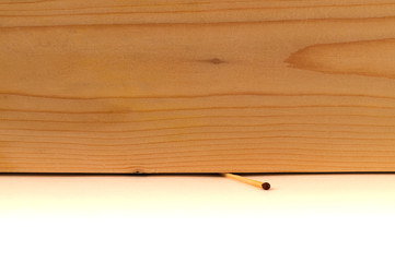 One thin match, crushed by a thick wooden board, a tree texture and a white background with a division along the border of the lower third of the image.