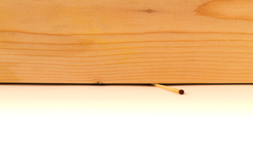 A match crushed by a thick wooden board, a wooden texture and a white background with a border in the center of the image.