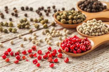 Different pepper in a wooden spoons on wooden table.