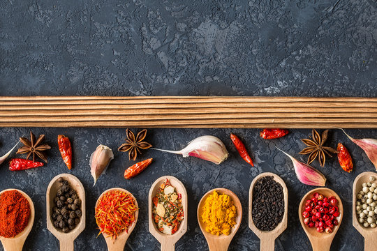 Various spices in spoons  on dark stone table.