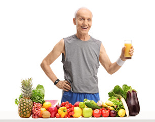 Obraz premium Elderly man holding a glass of juice behind a table with fruit and vegetables