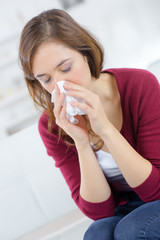 ill young woman is sneezing in a tissue