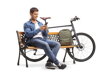 Young man with a phone and a bicycle sitting on a wooden bench
