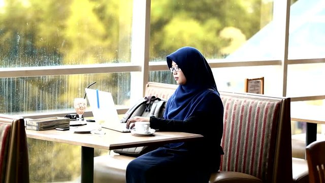 Muslim south east asian woman with hijab is typing and working on laptop computer at the cafe