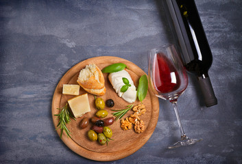Bottle and glass of wine with cheese, olives, bread, nuts and basil on dark background. Wine and food concept. View from above, top
