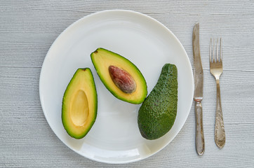 Fresh sliced avocados on the white plate. Healthy vegan diet food on gray background. Top view