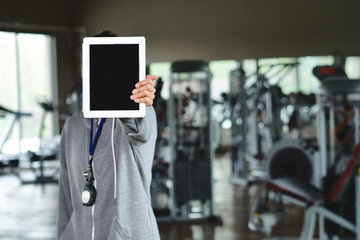 A young personal trainer (girl) holds a black board with the gym in the background. Concept: Sport, fintess, happiness.