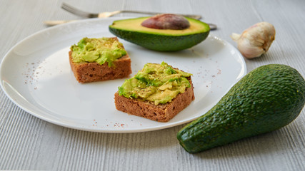 Vegan avocado toasts on the white plate with black salt and garlic. Vegetarian avocado sandwiches on the gray background. Close up view