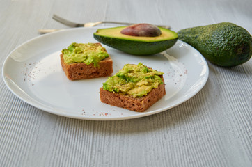 Tasty avocado toasts on the white plate with black salt and garlic. Vegetarian avocado sandwiches on the gray background with free copy space. Side view