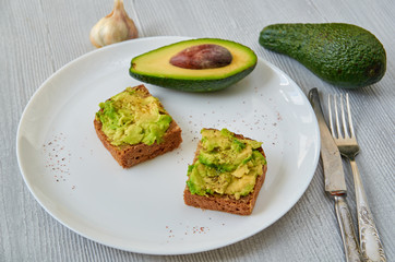 Tasty avocado toasts on the white plate with black salt and garlic. Vegetarian avocado sandwiches on the gray background with free copy space. General view